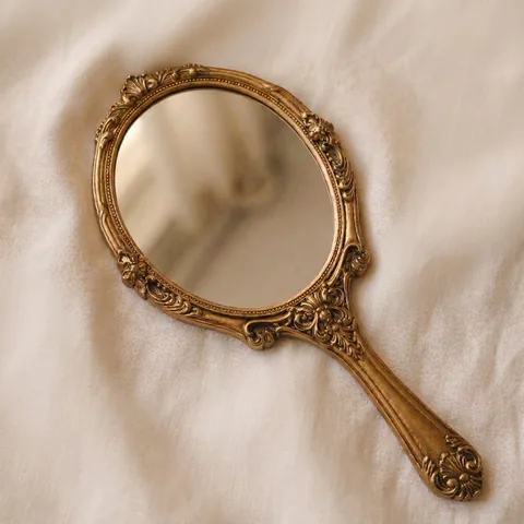 An antique gilded hand mirror resting diagonally on cream linen